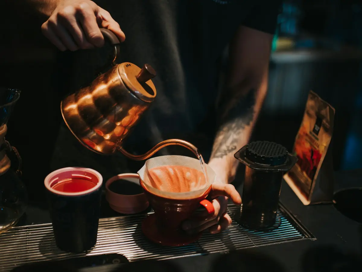 Barista pouring hot water from a copper kettle into a pour-over coffee filter